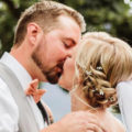 headshot of bride kissing her groom with a braid and flowers in her hair