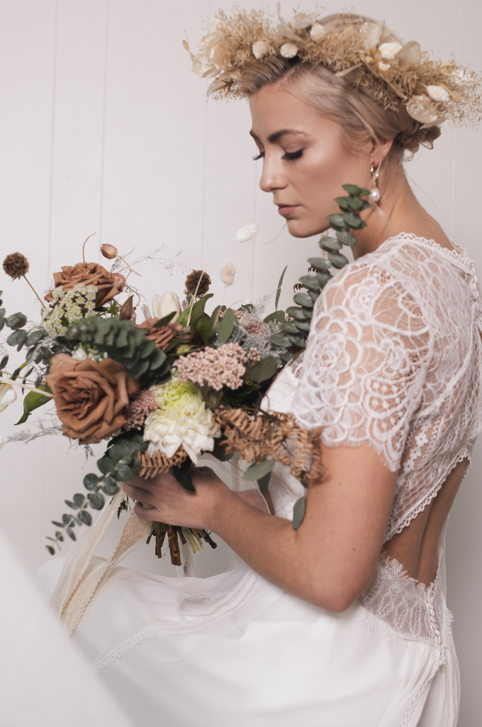 Bride with natural bridal makeup of warm toned browns and soft pinks holding an earth toned bouquet and wearing a bohemian inspired flower crown. Makeup by Top Notch Art of Makeup.