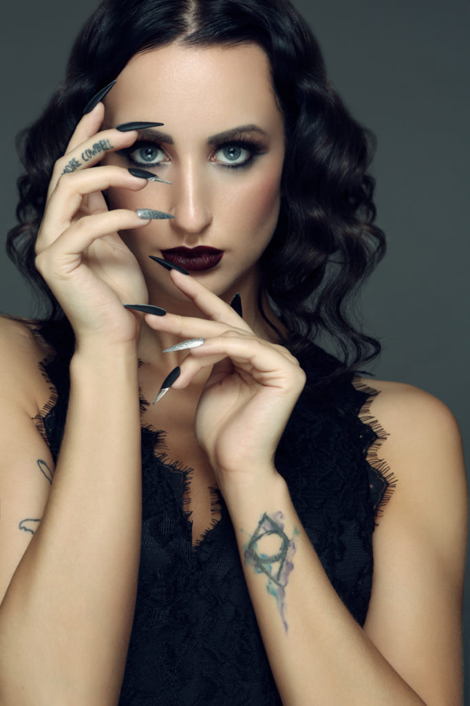 Portrait of model with dark moody makeup, hands in face with long dark nails. Makeup by Top Notch art of Makeup
