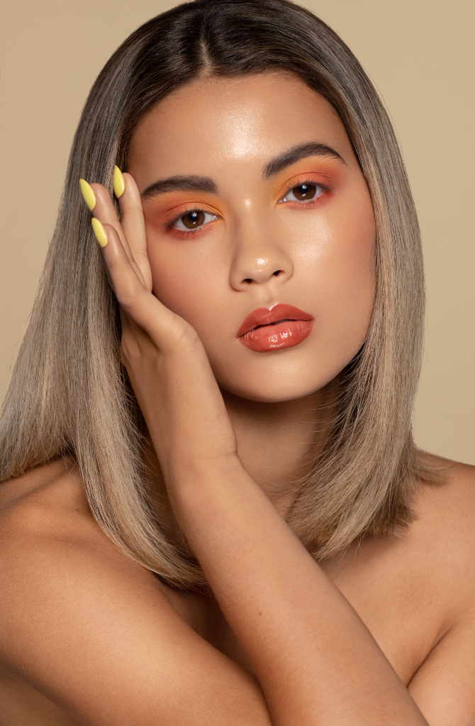 Creative makeup on model wearing yellow and orange eye shadow with coral coloured lilpstick. Model is touching face with yellow coloured nails. Makeup by Top Notch Art of Makeup.