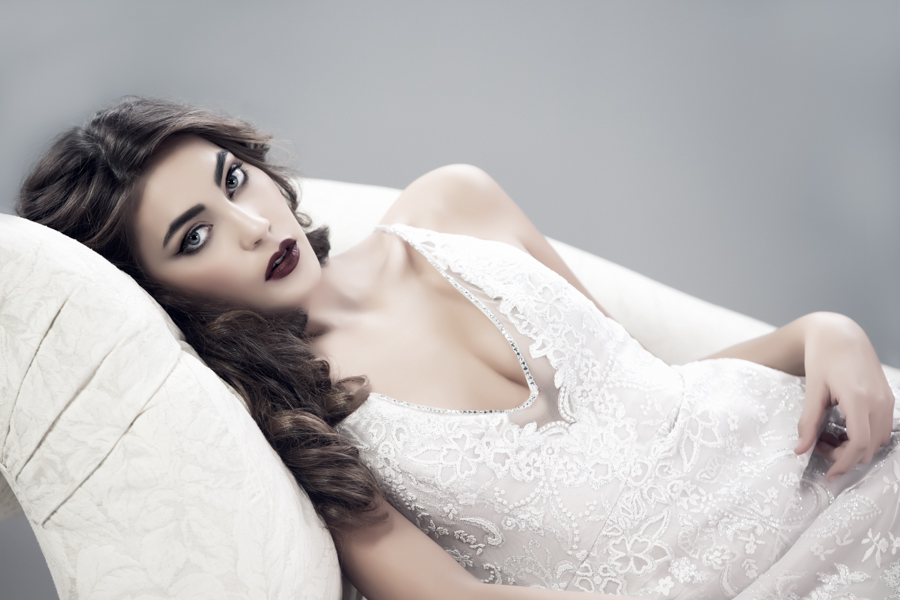Model lying on ivory couch in white wedding dress and dramatic dark makeup by Top Notch Art of Makeup