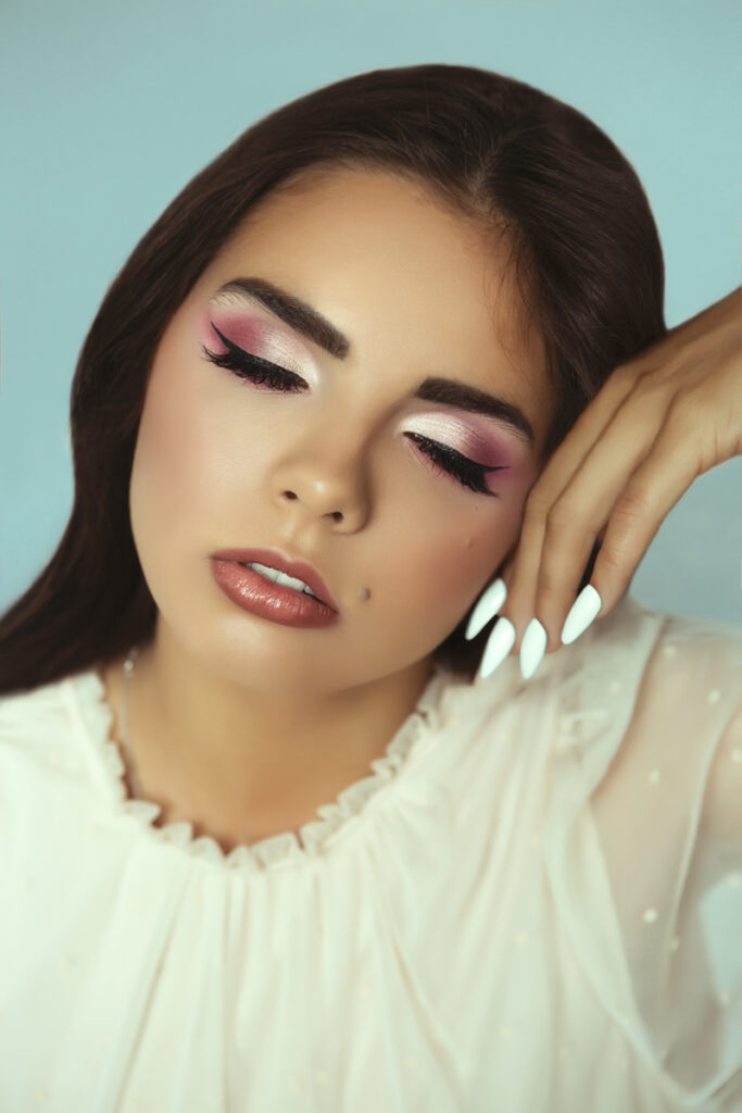 Model with closed eyes touching face. Bright pink and white eyeshadows on eyes.